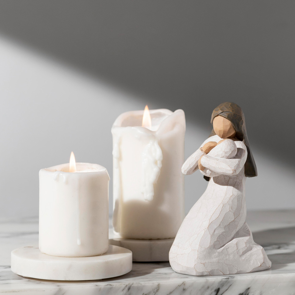 Figura de una mujer de pie con las manos en el corazón, acompañada de dos velas blancas encendidas sobre una superficie de mármol. Comunidad de vida