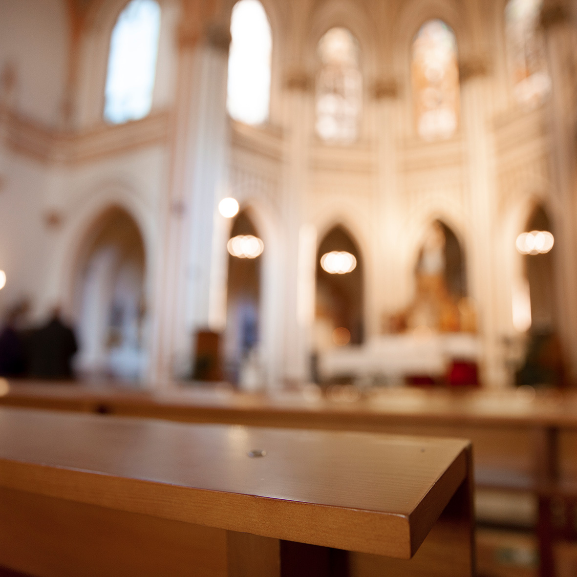 Interior blurry view of a church with wooden pews in the foreground and softly lit stained glass windows in the background. Prioridades Comunidad Stella
